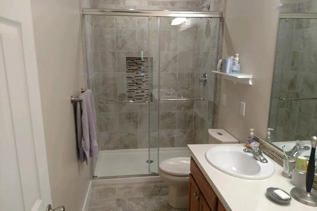 Bathroom after renovation with a sliding glass shower enclosure, large wall tiles, and the existing wood vanity.