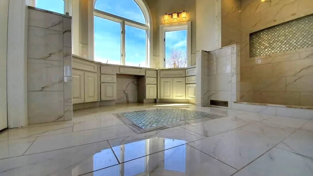 Primary bathroom after renovation with light floor tile, vanity cabinetry below the windows, and an enlarged shower area.