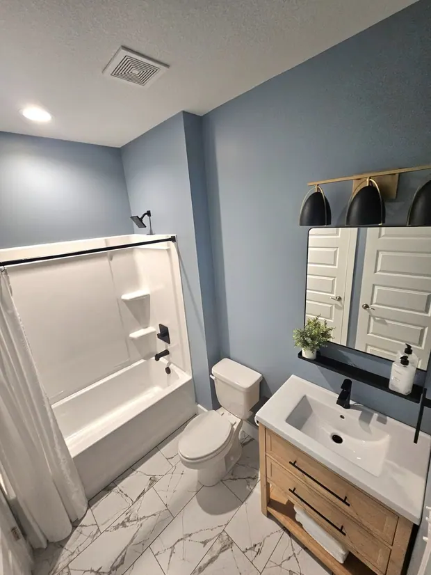 Renovated bathroom with blue walls, a wood vanity, patterned floor tile, and the retained bathtub.
