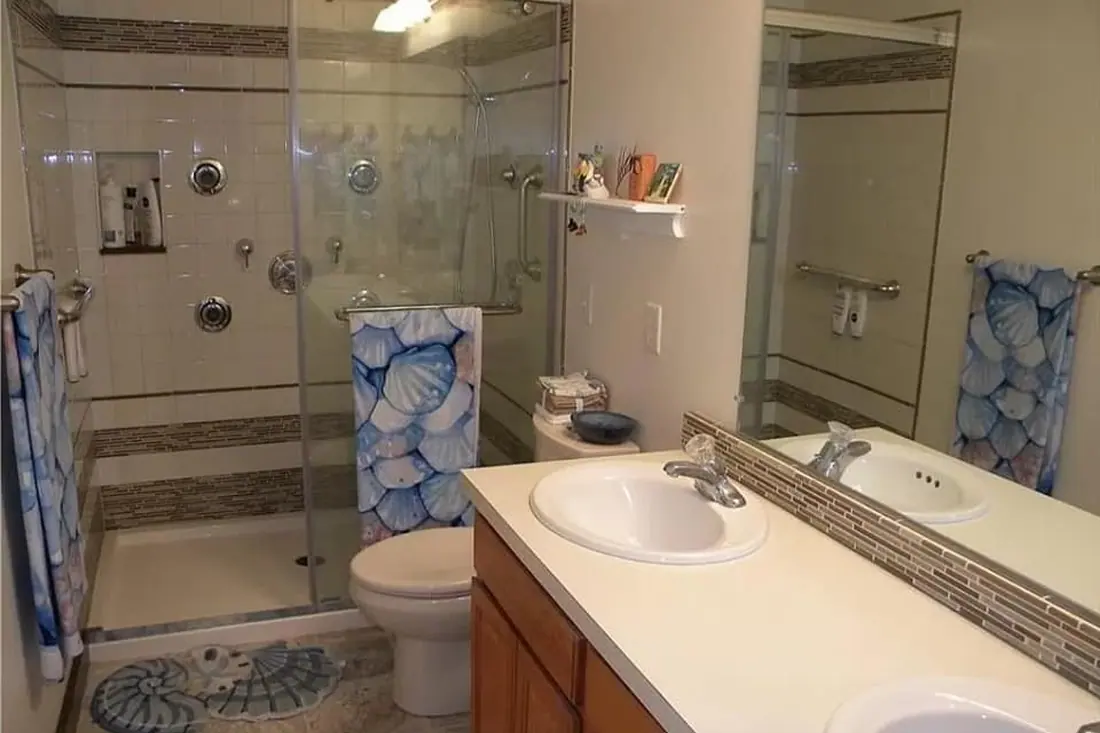 Bathroom before renovation with a glass corner shower, multiple wall fixtures, and a wood vanity.