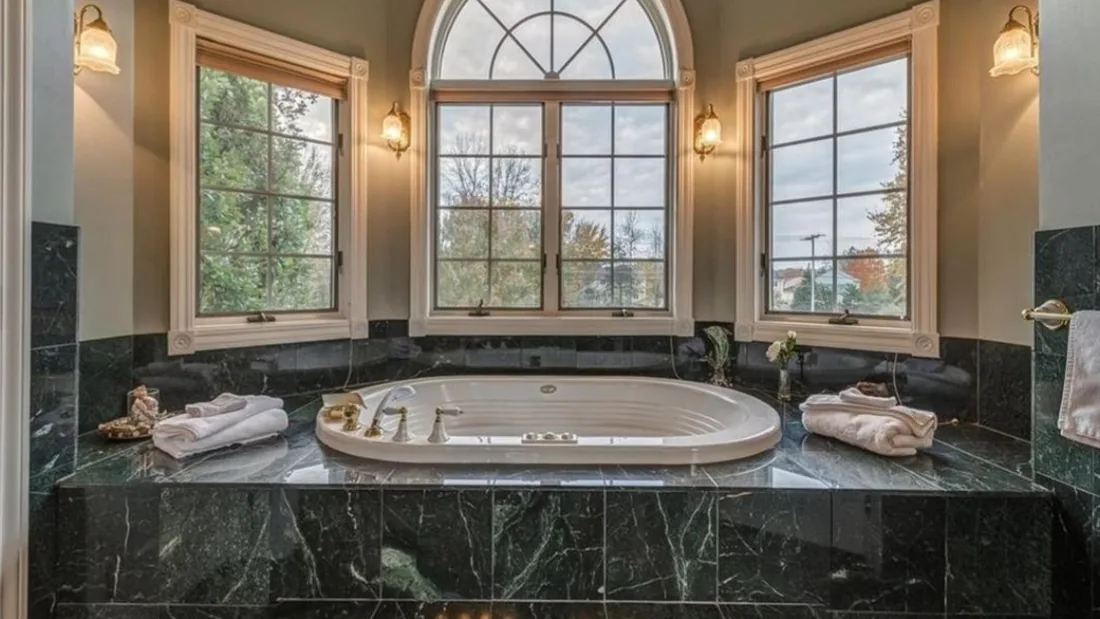 Primary bathroom before renovation with a built-in bathtub, green surround, and arched window.