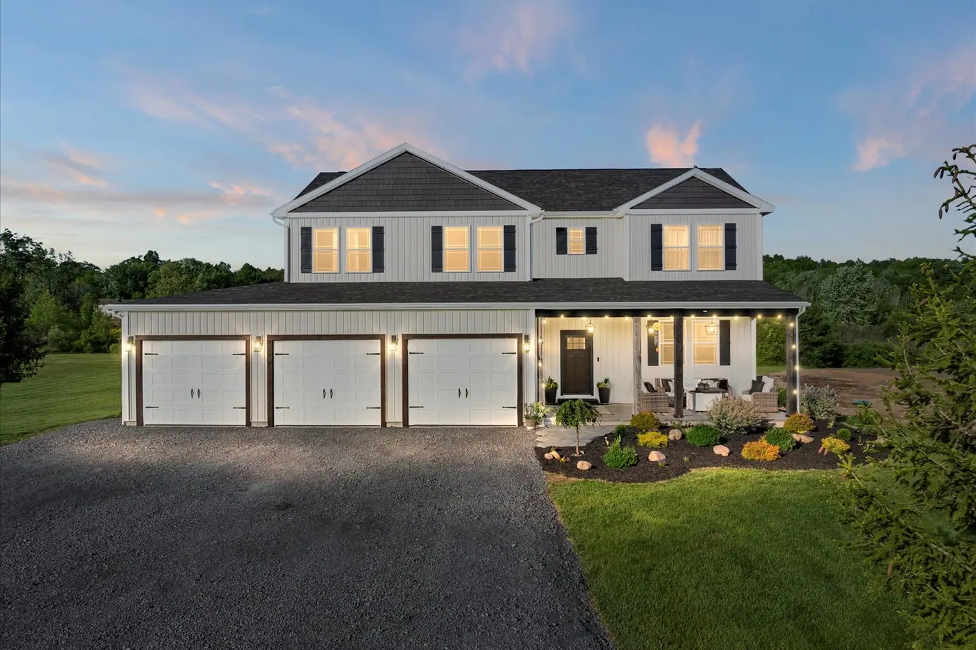 The finished house at dusk, with lit windows and a three-car garage