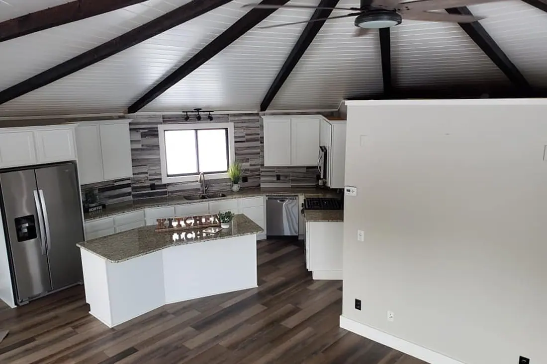 Renovated kitchen with white cabinetry, an island, dark exposed ceiling beams, and new flooring.