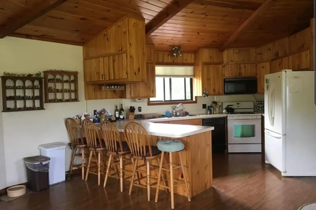 Kitchen before renovation with wood-paneled walls and ceiling, wood cabinets, and a peninsula.
