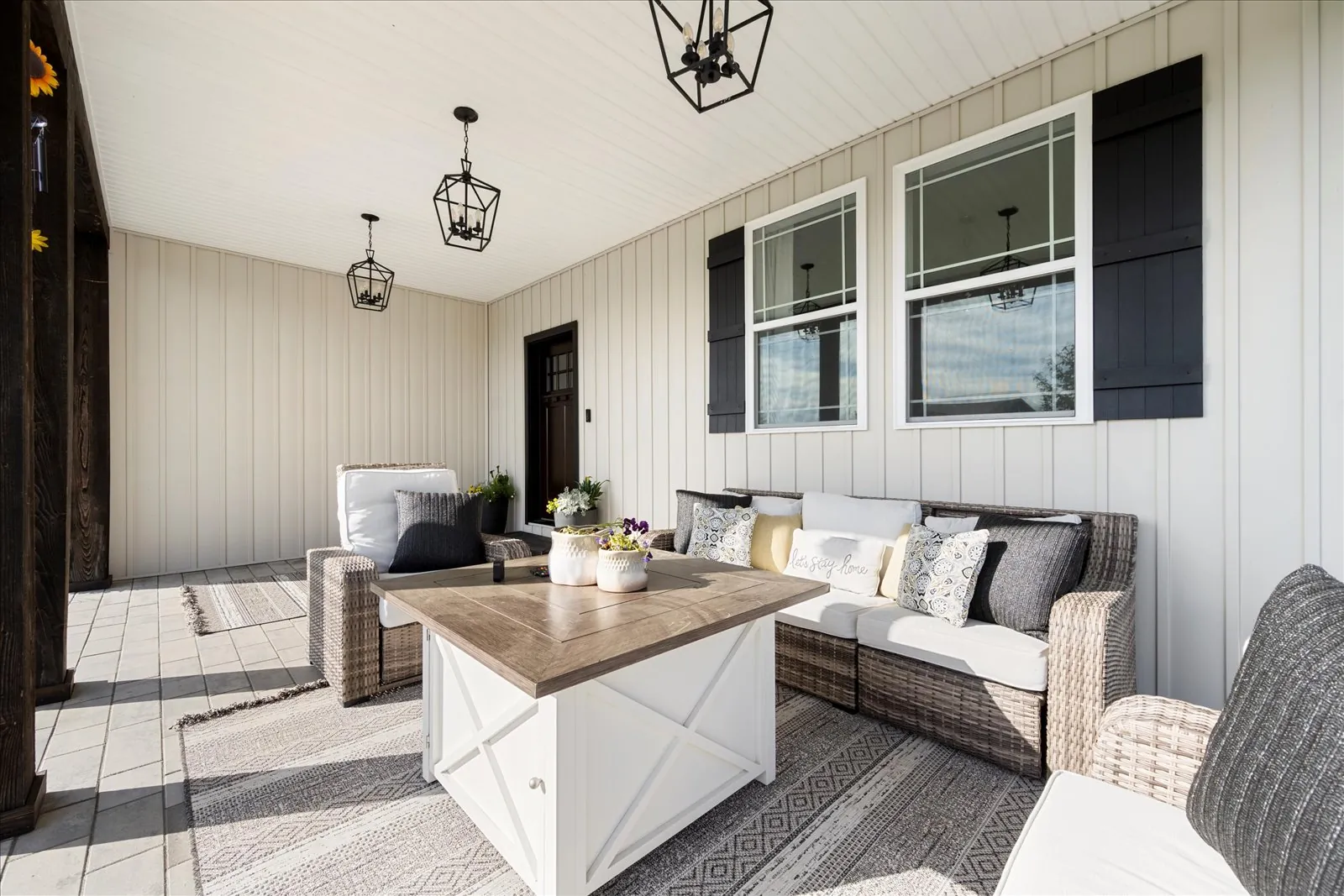 A covered porch built onto the back of the house, with wicker seating, lantern pendants and board and batten walls