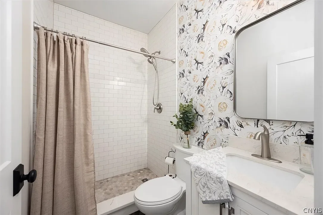 Bathroom with patterned wallpaper and a tiled tub surround in Central Square, NY.