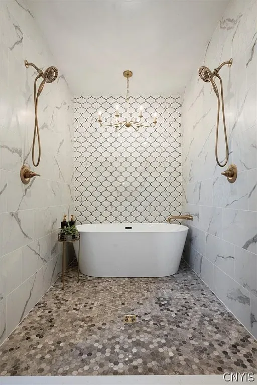 Freestanding bathtub and dual shower fixtures with a pebble floor in Central Square, NY.