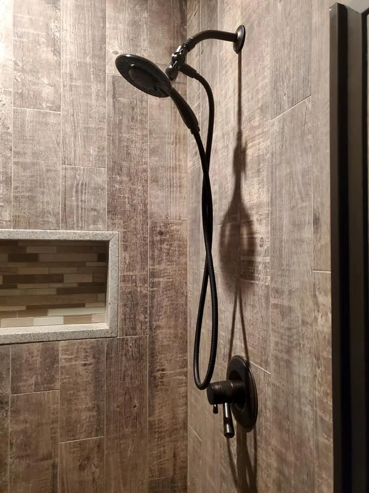 Wood-look shower tile with a recessed niche and dark fixtures in Central New York.