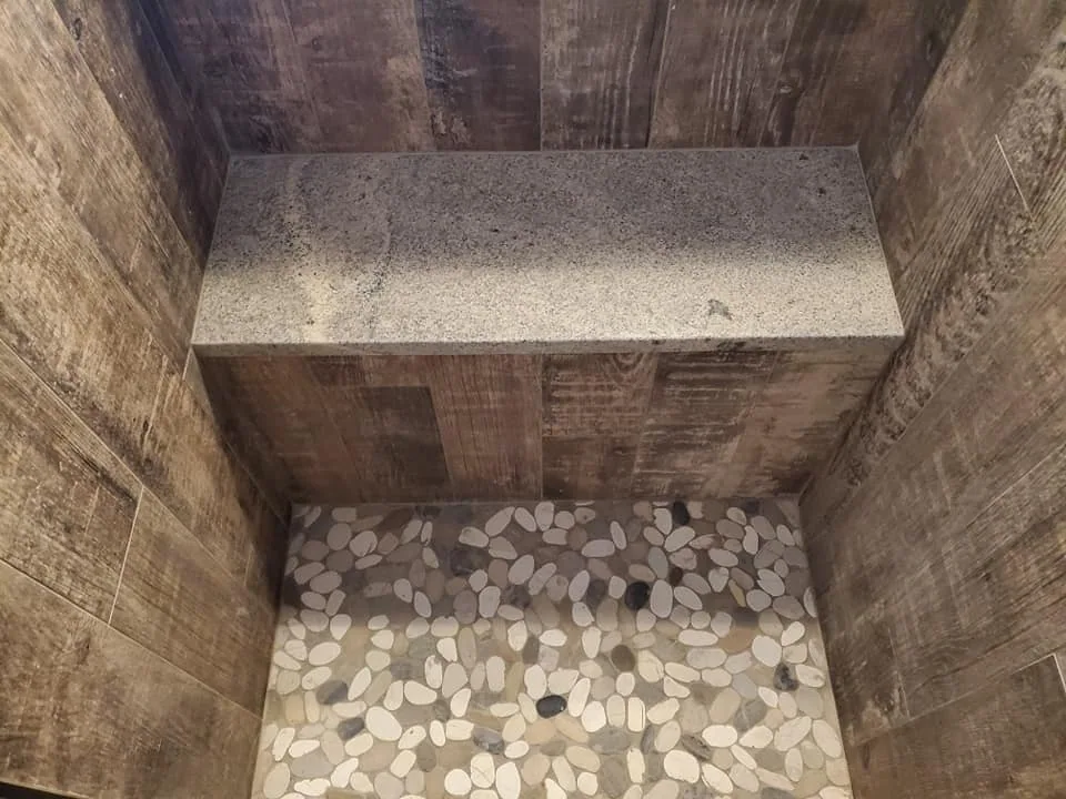 Stone shower bench above a pebble tile floor in Central New York.