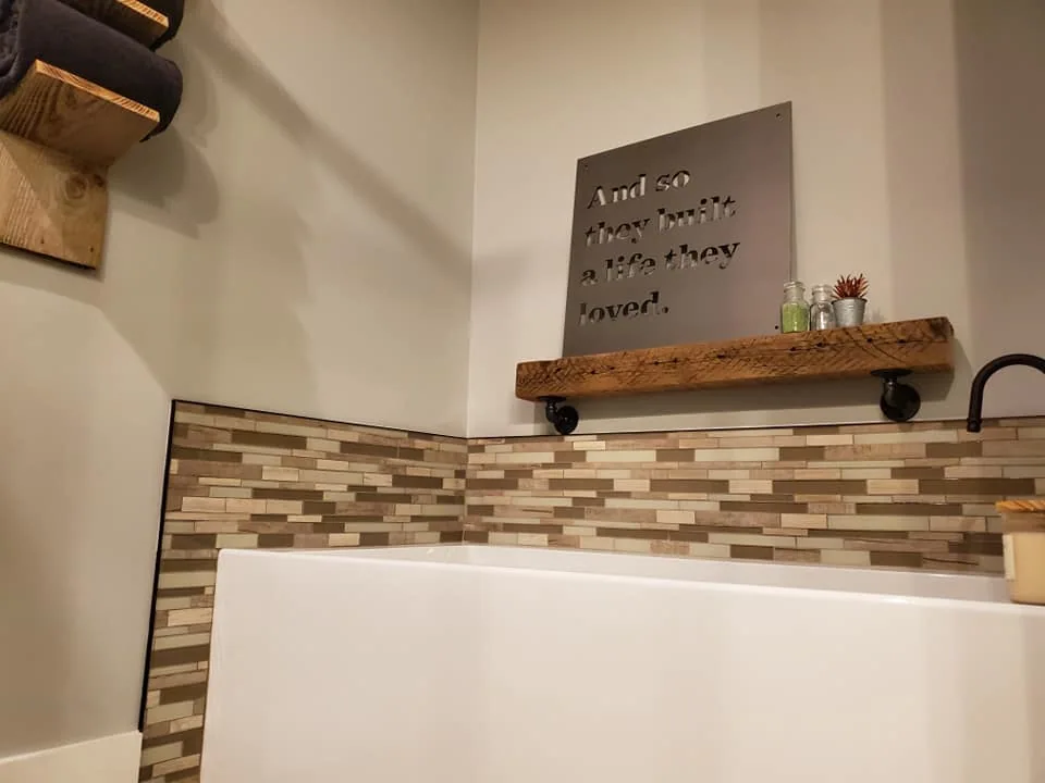 Bathtub with a mosaic tile border and wood shelf in Central New York.
