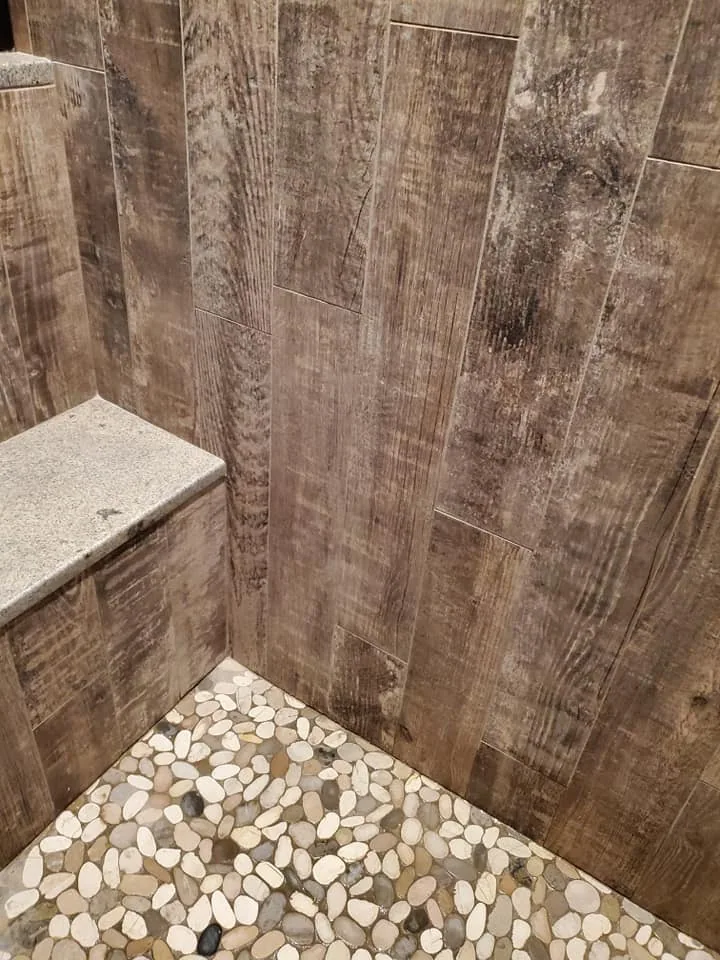 Pebble shower floor beside wood-look wall tile in Central New York.