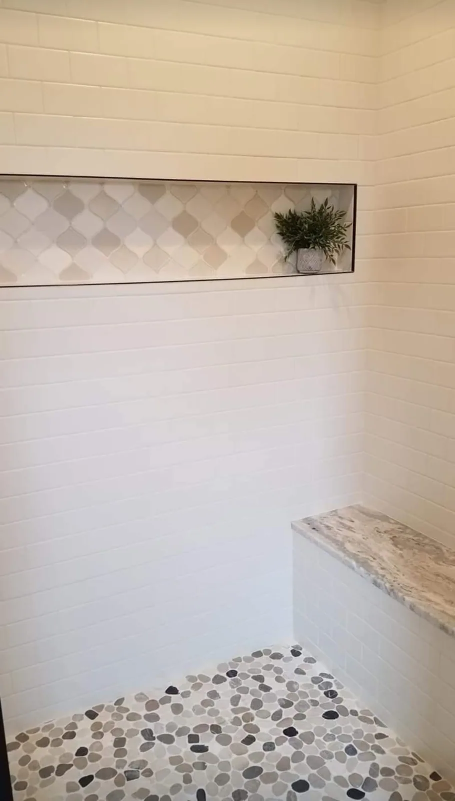 Tiled shower with a stone bench and pebble floor in Hastings, NY.