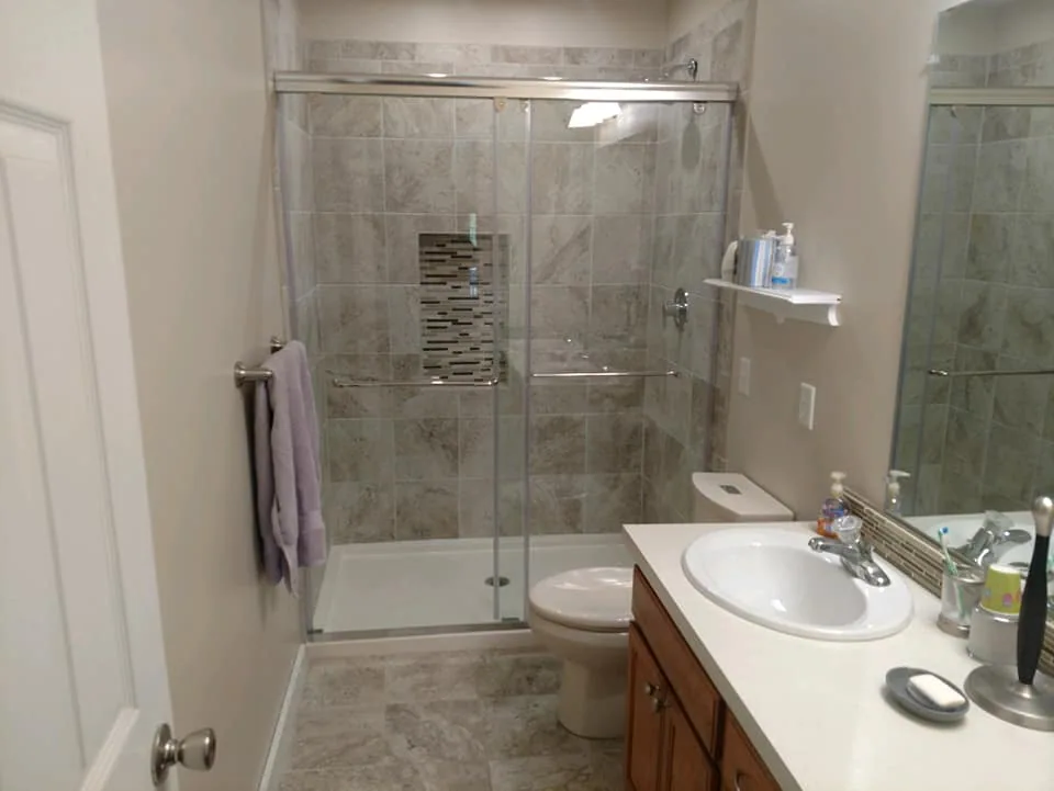 Rebuilt glass shower enclosure beside the retained wood vanity in Central New York.